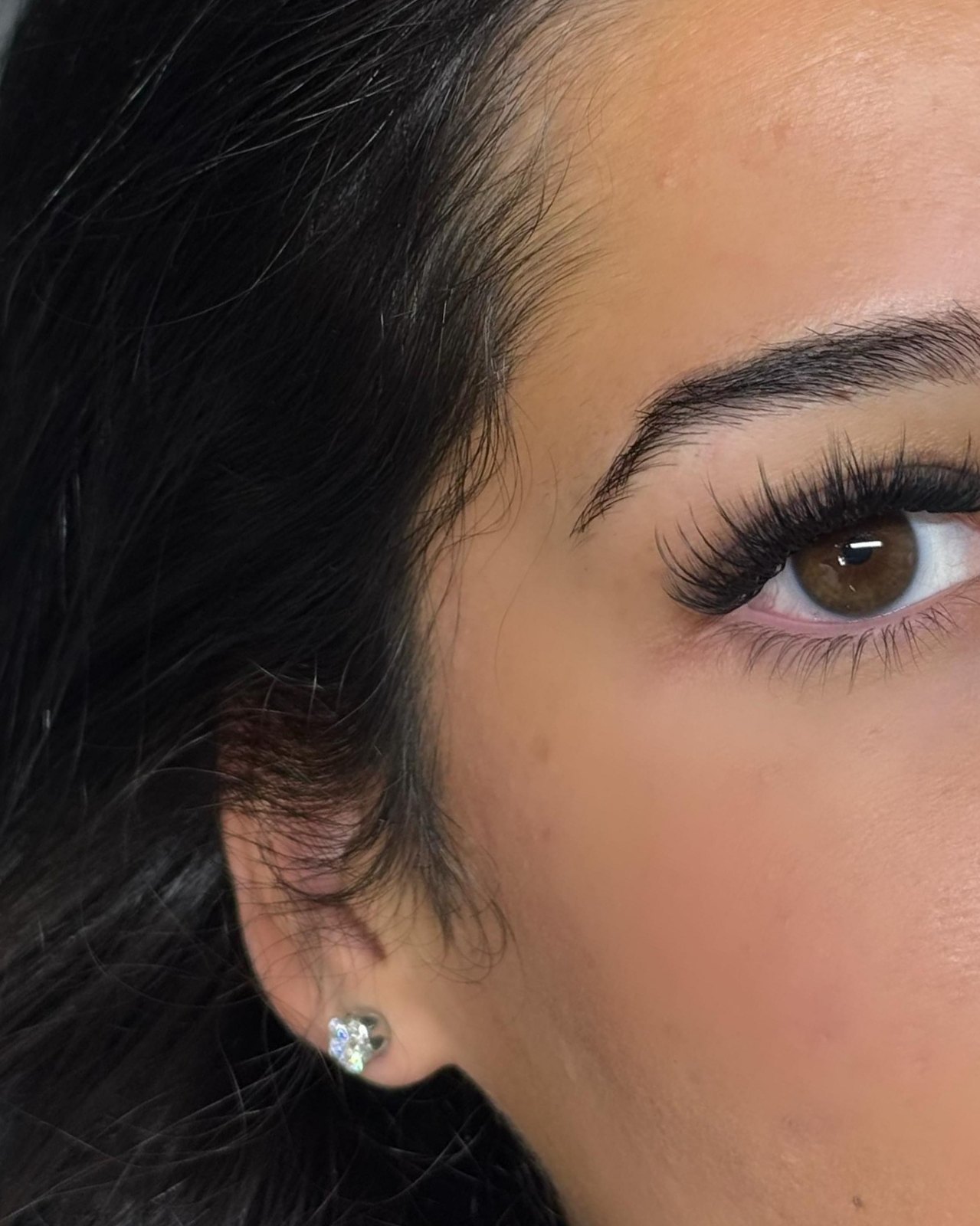 Volume wispy wimperset bij een klant met donker haar en een oorknopje